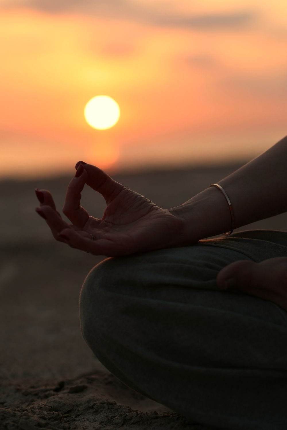 Hand in a meditation gesture in front of a setting sun